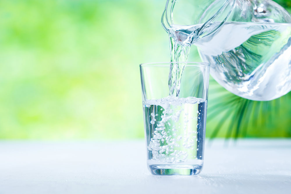 Schungit-Wasser wird aus dem Wasserkrug ins Glas eingeschenkt